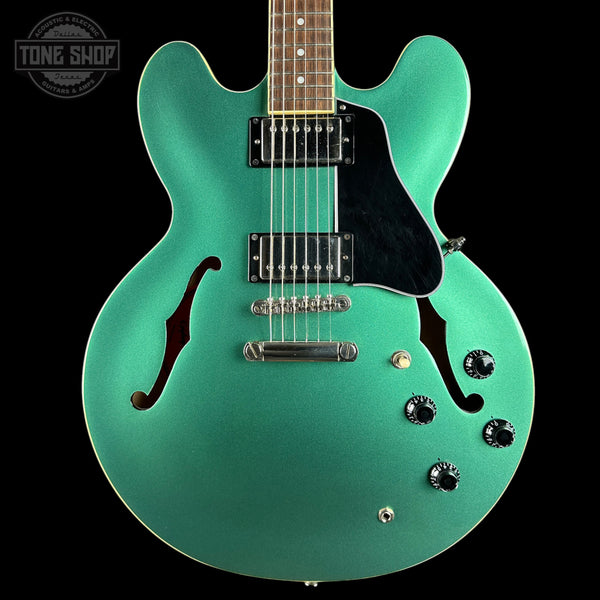 Turquoise electric guitar with a black pickguard on a black background, featuring 'Tone Shop' branding.