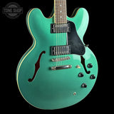 Turquoise electric guitar with a black pickguard on a black background, featuring 'Tone Shop' logo.