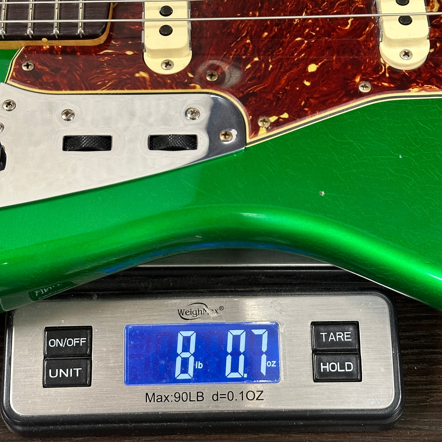 Green electric guitar next to a digital scale displaying weight