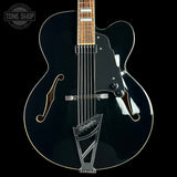 Black electric guitar with a clear coat on a black background, featuring the Tone Shop logo.