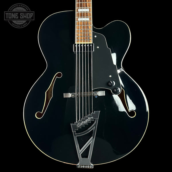 Black electric guitar with a clear coat on a black background, featuring the Tone Shop logo.