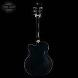 Back view of a black electric guitar on a black background with 'Tone Shop' logo.