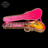 A sunburst electric guitar inside an open hard case with a bright pink interior, photographed against a solid black background. A Tone Shop watermark is visible in the top-left corner.