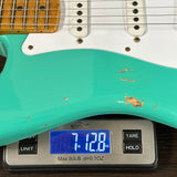 Teal electric guitar on a digital scale displaying weight.