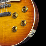 Close-up of a sunburst electric guitar body showing gold-toned control knobs, a black bridge, and a metal plate against a black background.