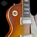 Close-up of a classic electric guitar body showing a sunburst finish, a gold-tone circular badge, a silver humbucker pickup, and part of the dark fretboard against a black background.
