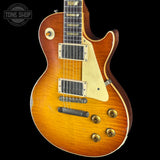 A classic electric guitar with a sunburst finish, featuring a warm orange-to-brown gradient, cream pickguard, and gold hardware, shown against a solid black background.