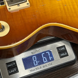 Close-up of a guitar body resting on a digital scale to measure weight, with the scale displaying 8.67 oz.