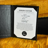 A Gibson Custom Certificate of Authenticity insert shown inside a black folder on a yellow faux-fur surface. The insert includes fields for base model, finisher treatment, finish, instrument serial number, and a Gibson Dealer Seal.