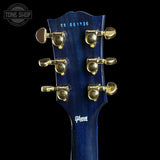 Close-up of the headstock of a Gibson electric guitar, showing a dark blue glossy finish with gold tuning pegs and a white Gibson logo on a black background.
