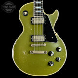 A Gibson Les Paul Custom electric guitar in a distressed olive green finish, featuring a black pickguard, chrome hardware, and a worn vintage patina on a black background.