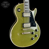 A classic electric guitar with a distressed olive green finish, featuring a black pickguard, chrome hardware, and gold-toned trim, shown against a solid black background.