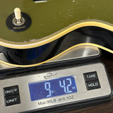 Close-up of an electric guitar body resting on a digital scale, with the scale display reading 9.42 oz.
