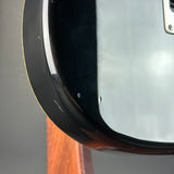 Close-up of the lower bout corner of a glossy black electric guitar body with a silver pickguard and a gold edge stripe, resting on a wooden surface.
