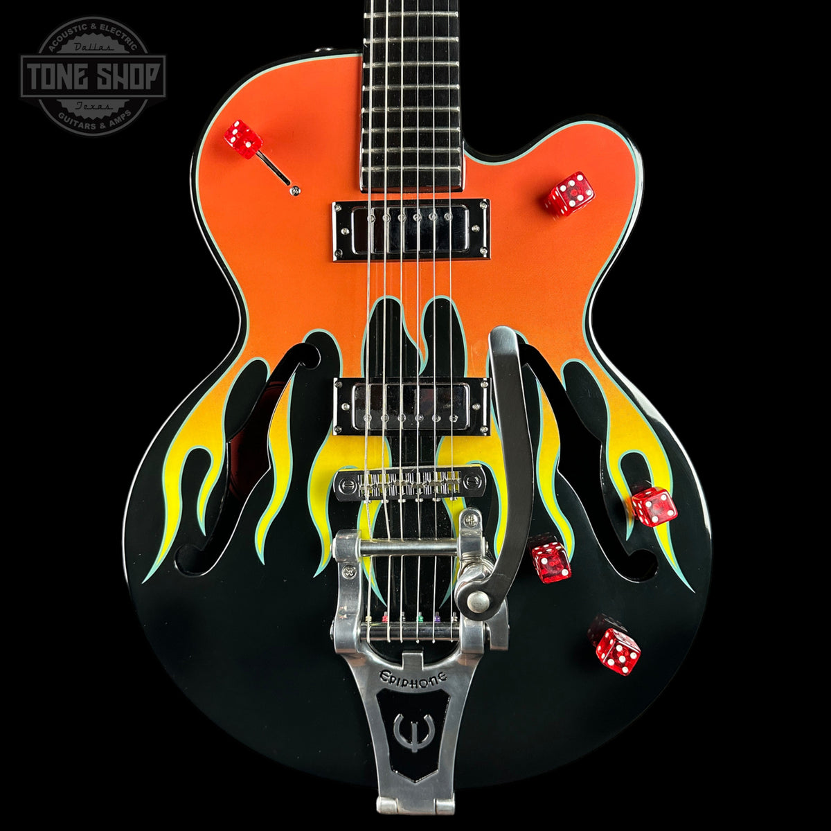 A custom electric guitar with a black body, a vibrant orange upper bout, and yellow and green flame decals. It features red double-sided dice as tuners and red die-cut stickers, photographed against a solid black background with a Tone Shop watermark in the top left corner.