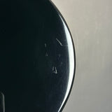 Close-up of a glossy black curved surface with visible scratches and scuffs against a light gray background.