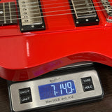 Red electric guitar on a digital scale displaying weight.