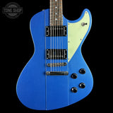 Blue electric guitar with a white pickguard on a black background, featuring the Tone Shop logo.