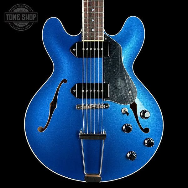 Blue electric guitar with a black pickguard on a black background, featuring the Tone Shop logo.