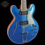 Blue electric guitar with a black pickguard on a black background, featuring the Tone Shop logo.