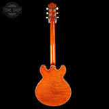 Back view of a wooden electric guitar on a black background with 'Tone Shop' logo.