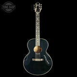 Acoustic guitar with a dark finish on a black background, featuring the Tone Shop logo.