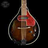 A close-up studio shot of a mandolin against a solid black background. The mandolin features a dark brown sunburst finish, a vibrant red and black marbled pickguard, gold-toned metal hardware, and a black headstock.