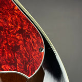 Close-up detail of a guitar body showing a red and orange flamed maple top, a silver control hole cover, and the edge of the instrument against a dark gray background.