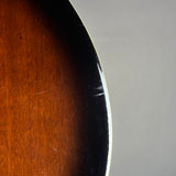 Close-up detail of a sunburst guitar body edge, showing the warm brown wood grain transitioning to black, with a light gray background on the right.