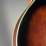 Close-up detail of a guitar body showing the dark center, a light cream binding edge, and a warm brown sunburst wood finish against a gray background.