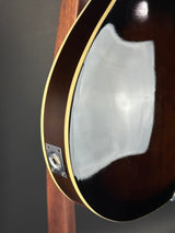 Close-up of the glossy dark brown body of an electric guitar, showing the edge with a light binding and a metal output jack near the lower left.