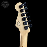 Close-up of the headstock of an electric guitar with a natural maple wood finish and black tuning pegs, shown against a solid black background. A Tone Shop watermark is visible in the top left corner.