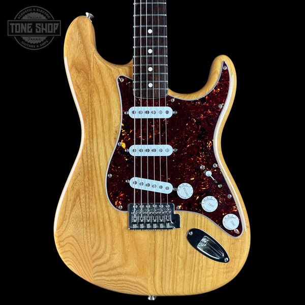 A classic electric guitar with a natural wood body, a dark red tortoiseshell pickguard, and a black neck, shown against a solid black background with a Tone Shop watermark in the top left corner.