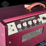 Close-up of a Magnatone Twilight Stereo guitar amp head with a textured burgundy red crocodile-embossed finish, cream control knobs, a dark brown control panel, and an orange-brown leather handle on a black background.