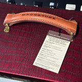 A close-up of a vintage-style Magnatone guitar amplifier or speaker cabinet in dark red croc-embossed material, featuring a tan leather handle with white stitching and brass hardware. A hanging tag reads 'TWILIGHTER STEREO' and lists specifications.