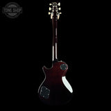 A dark reddish-brown electric guitar shown from the back against a solid black background, featuring a glossy finish, white hardware, and a white pickguard.