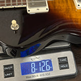 A close-up of an electric guitar body resting on a digital scale displaying 8.126 oz.