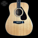 A natural wood acoustic guitar shown from the front against a solid black background, featuring a flamed maple top, dark pickguard, and black bridge. A Tone Shop watermark is visible in the upper left corner.