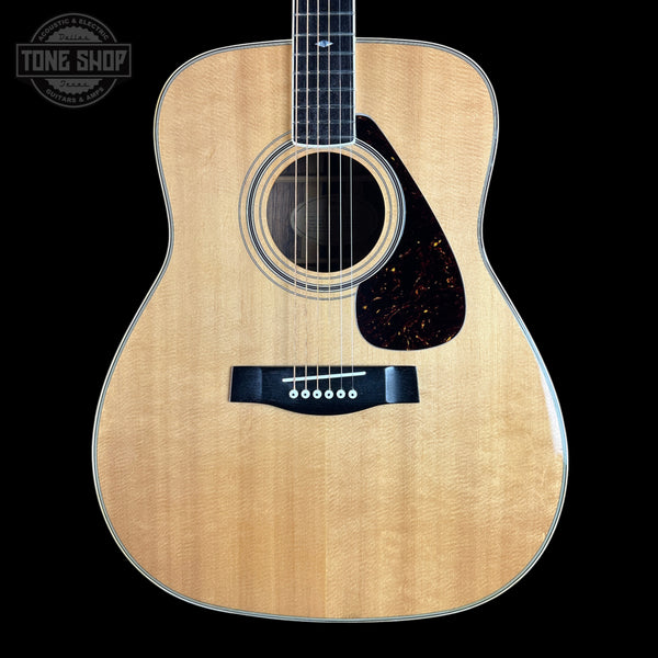 A natural wood acoustic guitar shown from the front against a solid black background, featuring a flamed maple top, dark pickguard, and black bridge. A Tone Shop watermark is visible in the upper left corner.