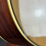 Close-up detail of an acoustic guitar body showing the dark brown wood grain, a cream-colored binding, and the light beige backplate.