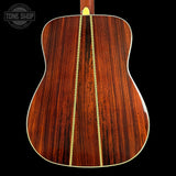 The back of an acoustic guitar made of rich, dark rosewood with a gold-colored metal tuner attached at the soundhole, set against a solid black background. A 'TONE SHOP' logo is visible in the top left corner.