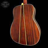 The back of an acoustic guitar made of rich, dark reddish-brown wood with two gold-toned inlay stripes down the center, shown against a solid black background.