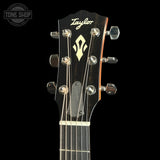 Close-up of a Taylor acoustic guitar headstock with six silver tuning pegs, six strings, and a black finish on a black background.