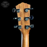 Close-up of the headstock of an acoustic guitar, showing six black Taylor tuning pegs on a warm brown wood backplate, set against a solid black background with a Tone Shop watermark in the top left corner.
