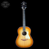 A Taylor acoustic guitar with a natural sunburst finish, shown from the front against a solid black background. The brand logo is visible on the headstock, and a 'TONE SHOP' watermark is in the top-left corner.
