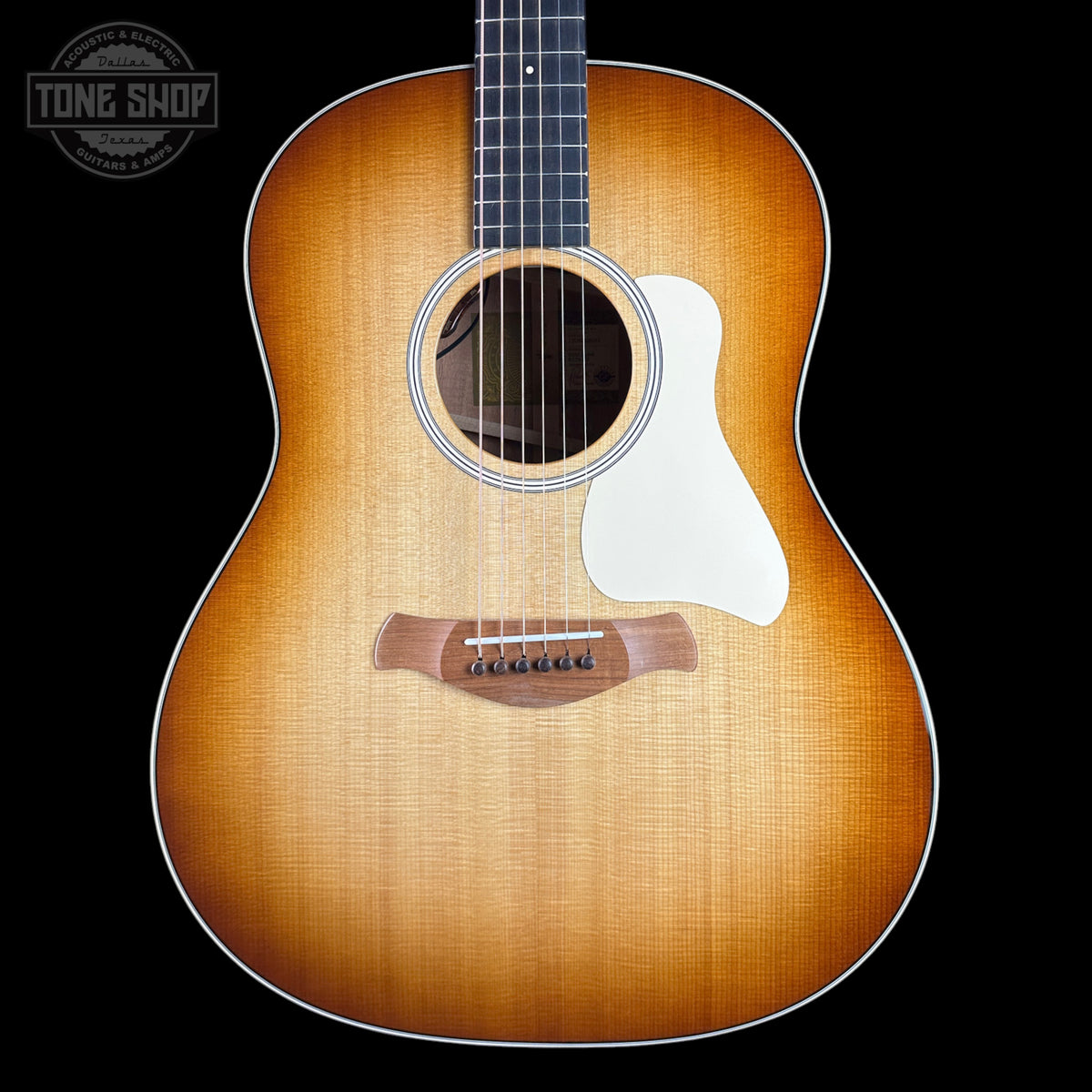 A front-facing acoustic guitar with a natural sunburst finish, featuring a white pickguard and a dark fretboard, shown against a solid black background with a Tone Shop watermark in the top left corner.