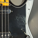 Close-up of a black electric guitar with visible wear and tear on the body.