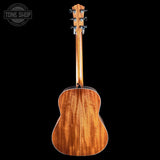 The back of a wooden acoustic guitar, showing a rich honey-toned wood grain finish, photographed against a solid black background with a Tone Shop watermark in the top left corner.