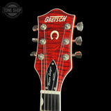 Close-up of a Gretsch Schumann Model acoustic guitar headstock, featuring a vibrant red flamed maple finish, silver tuning pegs, and white Gretsch branding on a black background.