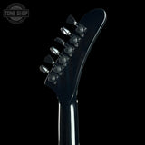 Close-up of the headstock of a glossy black electric guitar against a solid black background, showing the tuning pegs and a Tone Shop watermark in the upper left corner.